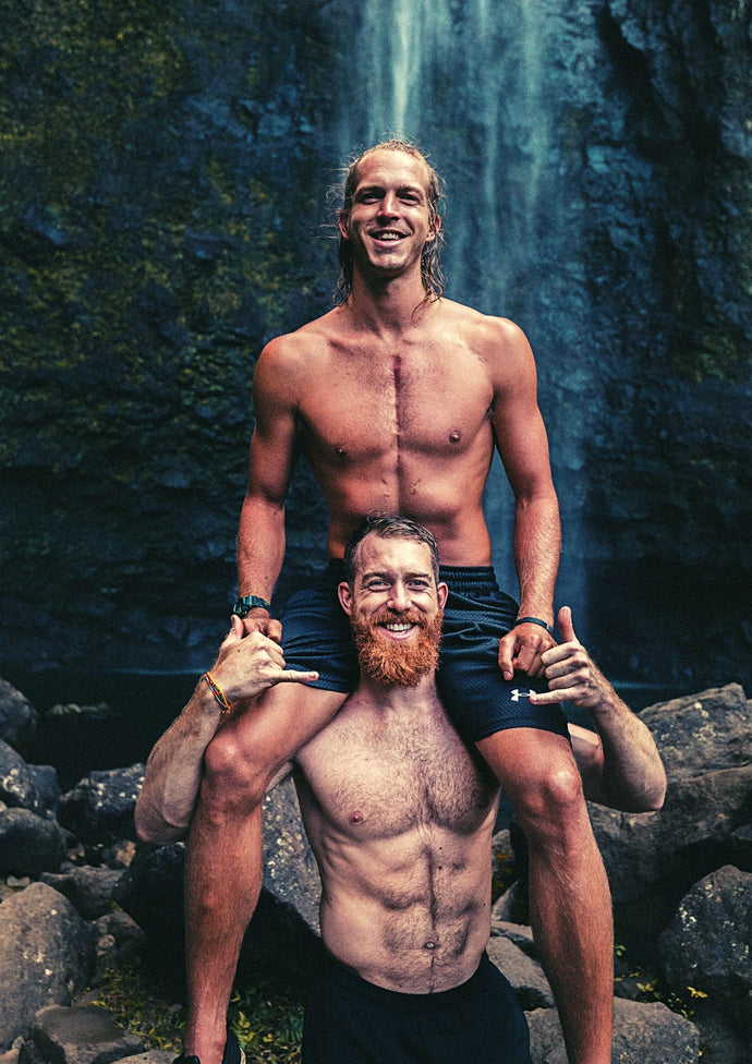 2 shirtless men in front of waterfall. Young men in 30s